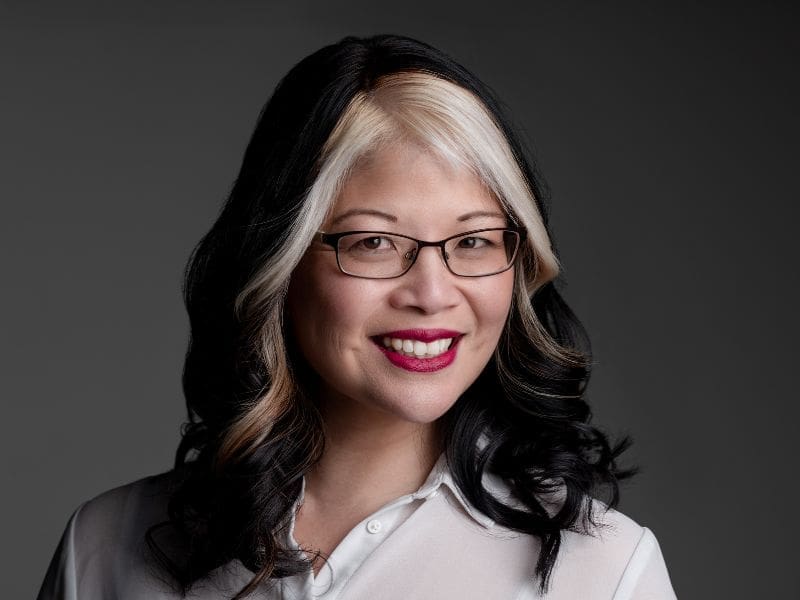 Woman with black and blonde hair weaaring a white shirt smiling at the camera