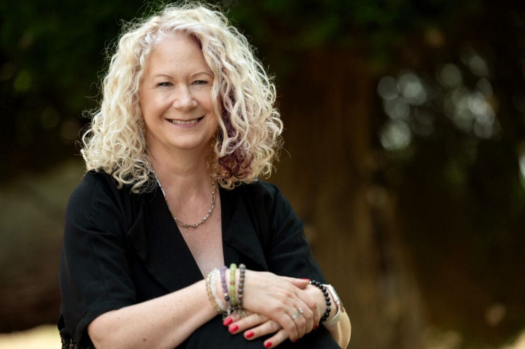 Woman with curly blonde hair and black shirt smilng at camera
