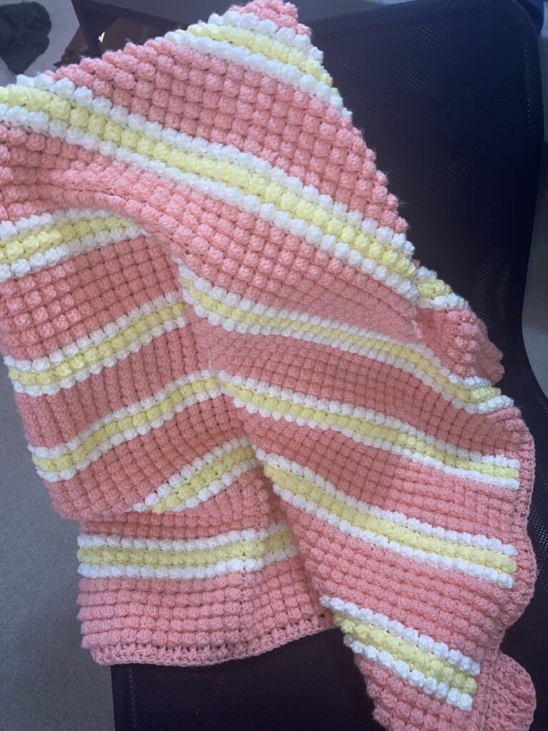 white, pink, and yellow crochet blanket across a black chair. 