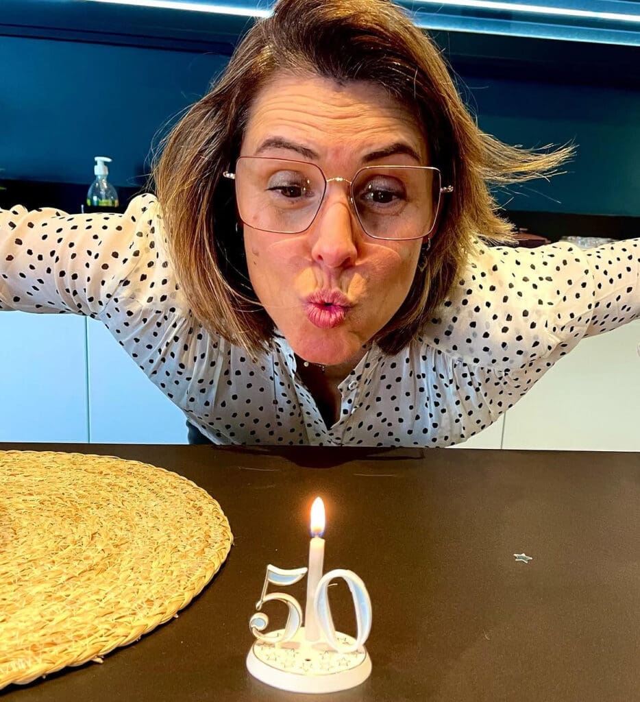 Woman with short brown hair blowing out candles with '50'