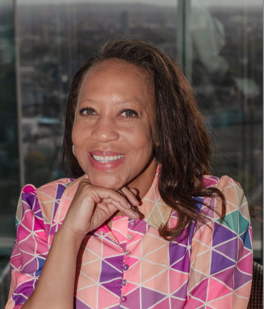 Woman in pink blouse, hand on chin, smiling at camera