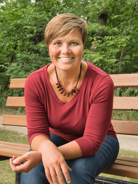 Photograph of Louise Sanders, sat on a bench with trees behind her and smiling