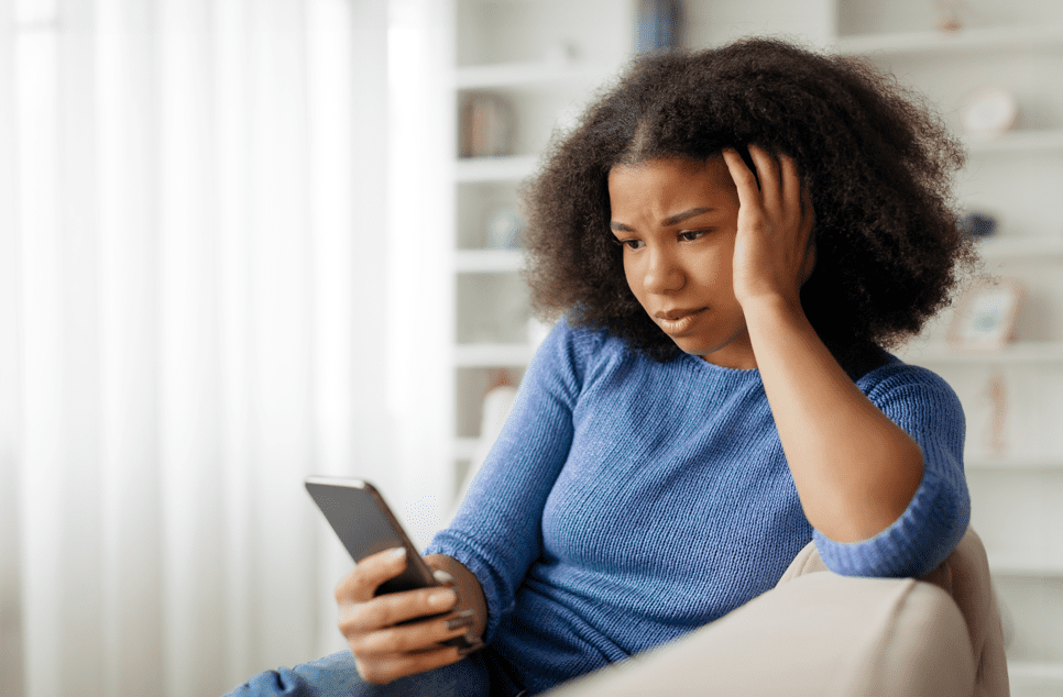 Concerned young woman looking at smartphone screen and touching head