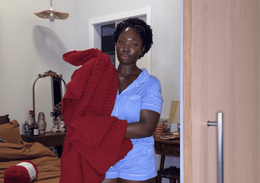 woman standing in blue sleepwear holding a red crochet blanket 