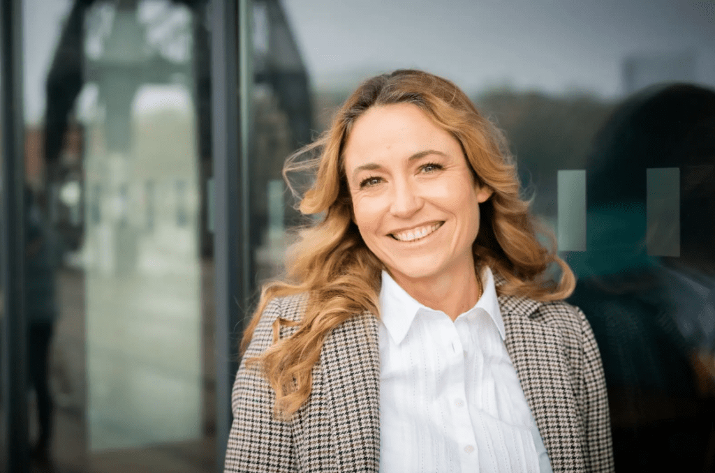Woman with blonde-brown hair in white shirt and blazer smiling at camera 