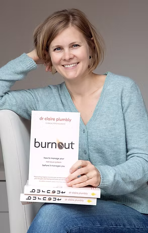 Woman with short blonde hair wearing a light blue sweater and holding a book 