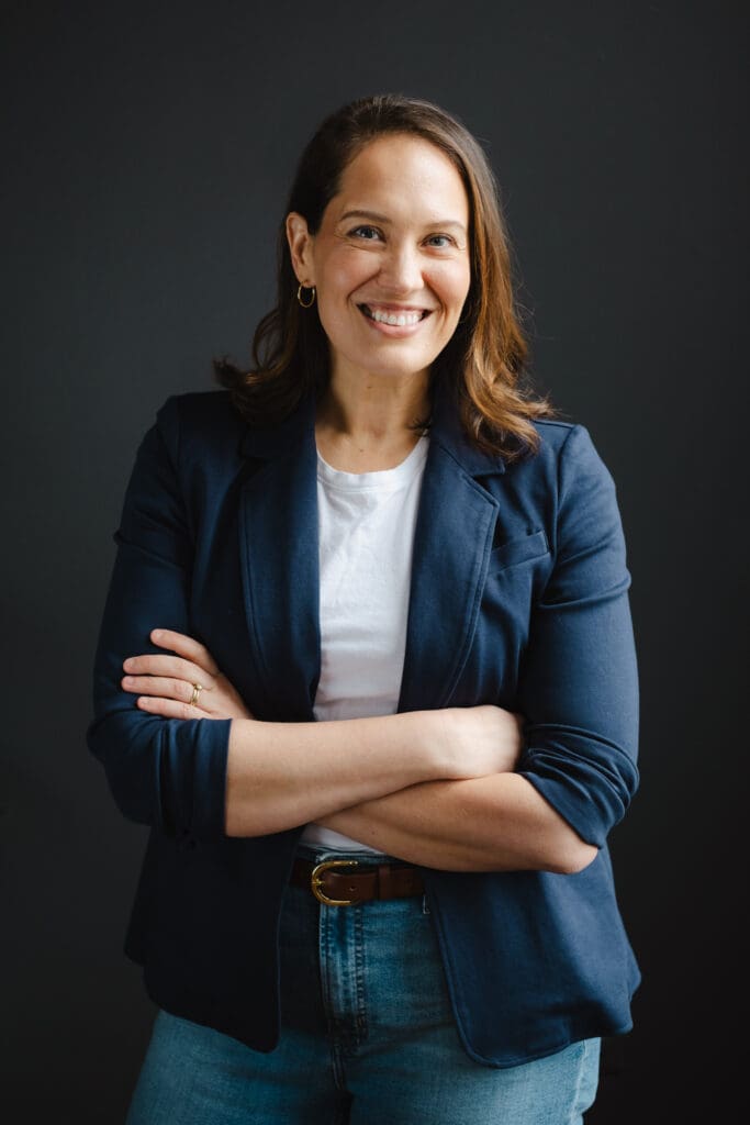 Woman wearing blue blazer, jeans, white shirt, arms crossed smiling at camera