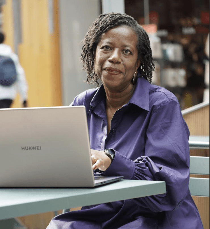 Woman sitting at table typing on laptop wearing a purple button down 