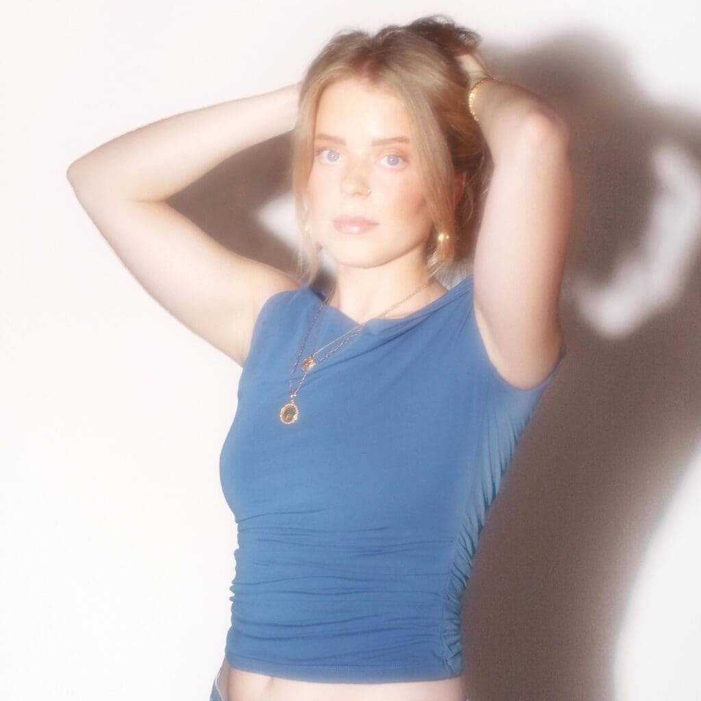Woman in cropped blue shirt, hands on head