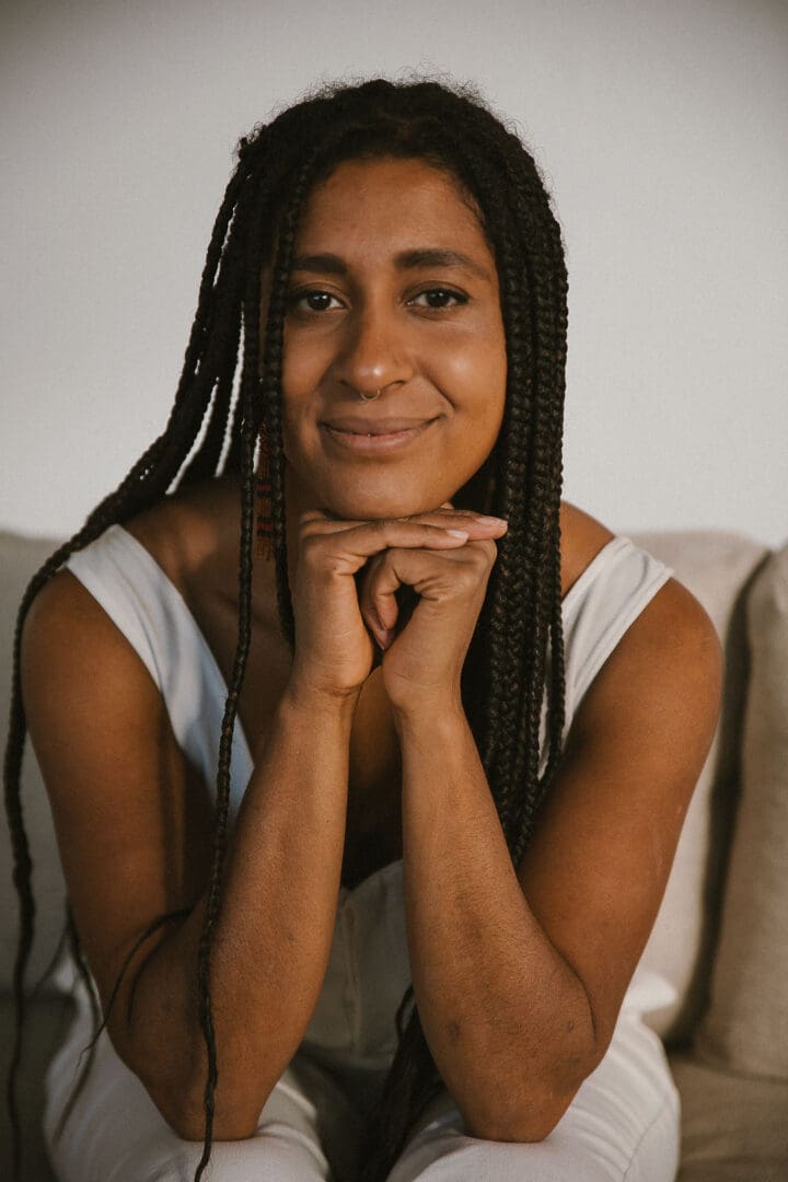 Woman wearing white outfit, long hair, hand under chin, smiling for photo. 